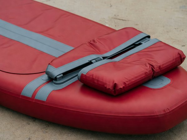 Close-up photograph of a deflated crimson and grey inflatable paddleboard showing the hinged split US fin box and double-layer rail tape