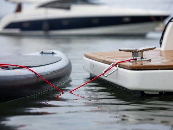 Close-up shallow depth of field photo of a floating red line clipped to a stainless steel D-ring on a paddleboard beside a wet yacht swim platform